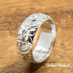 a silver ring with flowers on it sitting on top of a wooden table next to a pen