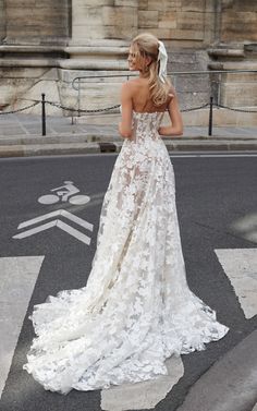 a woman in a wedding dress is standing on the street with her back to the camera