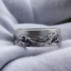 a wedding band with mountains etched on the side, sitting on top of a white blanket