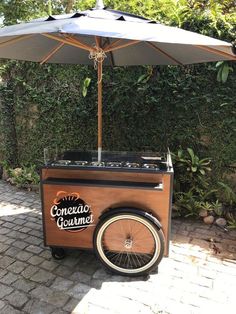 an old fashioned ice cream cart on the side of a brick road with an umbrella over it