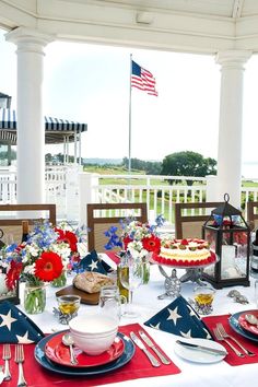 an outdoor dining area with american flags and patriotic decorations on the table, along with wine bottles and glasses