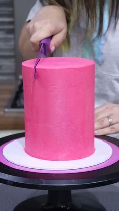 a woman is decorating a pink cake with purple icing on the top and bottom