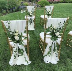 the chairs are decorated with white flowers and greenery for an outdoor wedding ceremony in the grass