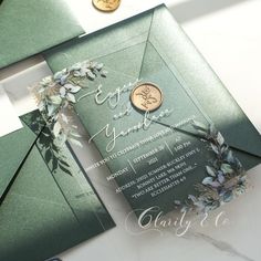 a green and gold wedding card on top of a white table with some coins next to it