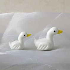 two white ducks sitting on top of a bed next to each other in front of a sheet