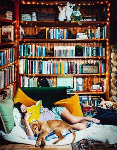 a person laying on a bed with a dog and bookshelf in the background