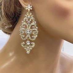 a close up view of a woman's face wearing gold earrings with crystal stones