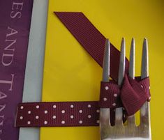 a fork and knife on top of a table with a purple ribbon around the forks