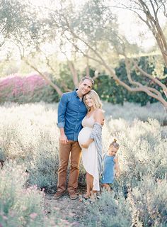 a man and woman standing in the middle of a field with their baby bump up