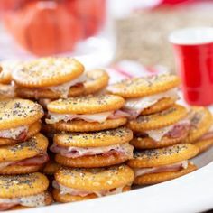 a white plate topped with crackers covered in cheese and ham sandwich sandwiches next to a red cup