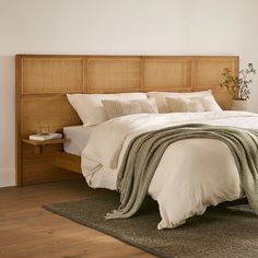 a bed with white linens and pillows in a small room next to a wooden headboard