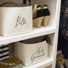 two white baskets with black lettering on them and some gold purses in the background