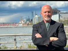 a man with his arms crossed standing in front of the water and cityscape