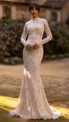 a woman in a long sleeved wedding dress posing for the camera with her hands on her hips