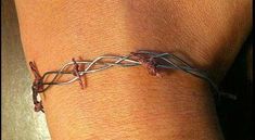 a close up of a person's arm wearing a bracelet with barbed wire on it