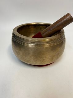 a metal singing bowl with a wooden stick sticking out of it's top, on a white surface