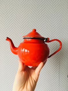 a hand holding a red teapot on top of a white tableclothed wall