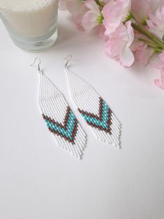 Step into the season with style with our white long beaded earrings, meticulously crafted with precision and care. Inspired by Native American artistry, these earrings feature a bold chevron pattern highlighted with turquoise and brown accents, making them a perfect complement to any Western-style ensemble. The fringe design adds a dynamic touch of movement, ideal for accentuating your summer look. These dangle earrings exemplify boho chic jewelry at its finest, offering both elegance and a whim White Fringe Earrings For Summer, White Beaded Fringe Long Drop Earrings, White Long Drop Earrings With Colorful Beads, White Long Drop Beaded Fringe Earrings, White Long Drop Jewelry With Beaded Fringe, White Bohemian Fringe Earrings, White Bohemian Beaded Earrings With Tassels, White Round Beaded Tassel Jewelry, White Tassel Jewelry With Round Beads