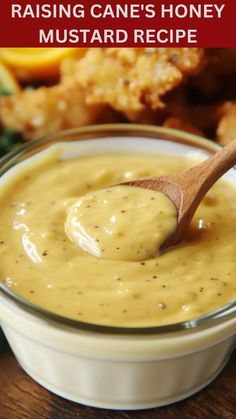 a wooden spoon in a small bowl filled with mustard sauce and chicken wings on the side