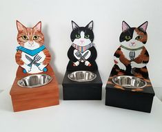 three cat figurines sitting next to each other on top of a wooden stand