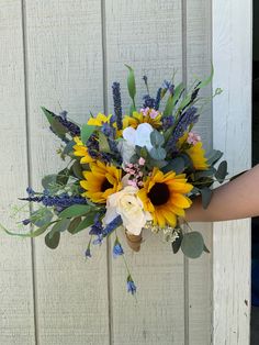 a bouquet of sunflowers and other flowers is held up against a white wall