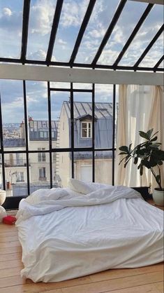 an unmade bed sitting on top of a hard wood floor next to a window