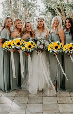 a group of women standing next to each other wearing dresses and holding sunflowers