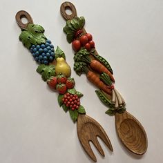 two wooden spoons with fruit and vegetables on them sitting next to each other,