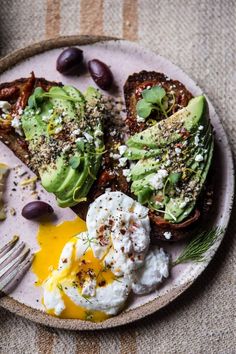 an avocado toast with sour cream and olives on a plate next to a fork