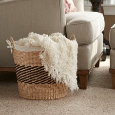 a basket sitting on the floor in front of a couch with pillows and blankets next to it