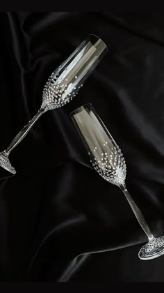 two champagne flutes are sitting on a black satin surface with beaded trimmings