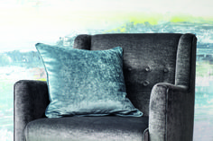 a gray chair with a blue pillow on it in front of a colorful wall mural