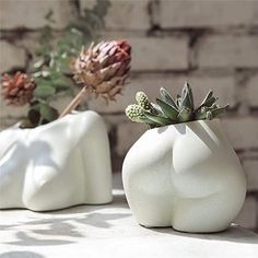 two white vases with plants in them sitting on a table next to a brick wall