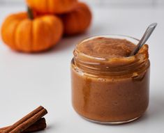 a glass jar filled with peanut butter next to cinnamon sticks and small pumpkins in the background