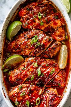 chicken with chili sauce and limes in a white casserole dish on a marble surface