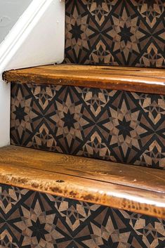 an old wooden stair case sitting on the side of a set of stairs with black and brown patterned wallpaper