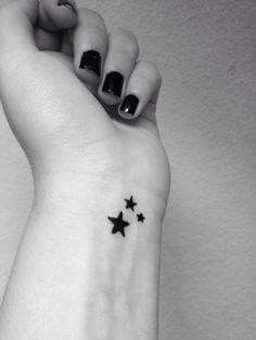 a black and white photo of a woman's wrist with three stars on it