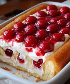 a piece of cake with cherries on top in a white dish sitting on a table