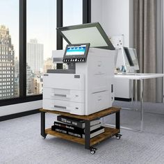 a large white printer sitting on top of a wooden table in front of a window