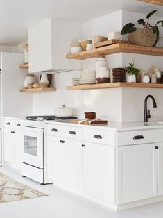 a white kitchen with open shelving above the stove and counter tops, along with potted plants