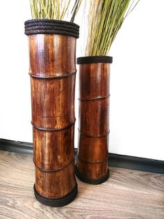 two wooden vases with grass in them sitting on a wood floor next to each other