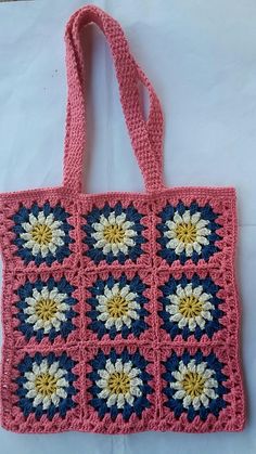 a pink crocheted bag with white and yellow flowers on the front is sitting on a table