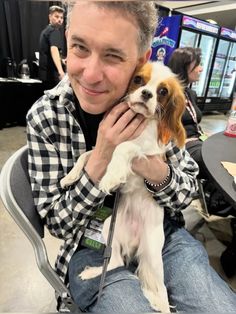 a man sitting in a chair holding a small brown and white dog on his lap