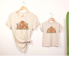 "This Mommy and Me Mama Pumpkin and Mini Pumpkin T-Shirt set is perfect for fall festivities! The t-shirts feature a cute pumpkin design, with \"Mama Pumpkin\" on the adult shirt and \"Mini Pumpkin\" on the child's shirt. Made from comfortable, breathable material, these shirts are great for family outings or cozy nights in. The set is available in various sizes to ensure a perfect fit for both mother and child. Show off your love of autumn with these adorable matching shirts! Key features: - Cute pumpkin design - \"Mama\" on adult shirt - \"Mini\" on child's shirt - Comfortable material - Available in various sizes How to order: 1. Select  Color 2. Select Size/Style 3. Add to Cart 4. If looking to purchase multiple sizes/colors repeat steps 1-3  5. Proceed to Check Out Please take a look Family Letter Print Tops For Fall, Casual Family T-shirt For Fall, Fall Tops With Letter Print, Fall Family Matching Crew Neck Tops, Fall Family Outfits, Sweatshirts Cute, Family Outings, Fall Festivities, Matching Sweatshirts