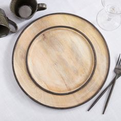 an empty wooden plate and two silverware on a white tablecloth with wine glasses