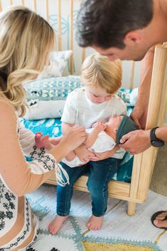 a man holding a baby in his hands while he is sitting on a bed with other people around him