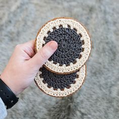 a hand holding two crocheted coasters on top of a gray carpeted floor