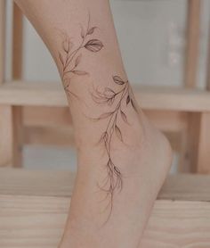 a woman's foot with a flower tattoo on the side of her leg, sitting on a wooden bench