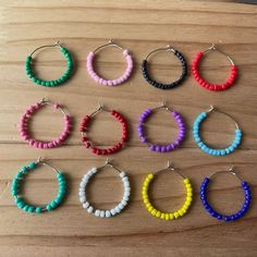 six pairs of beaded hoop earrings sitting on top of a wooden table next to each other