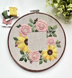 a close up of a cross stitch hoop with flowers on it and some spools of thread next to it